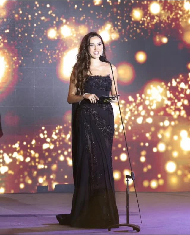 Host Elsa Zgheib stands at a microphone with a CAEL presentation card in 2025.