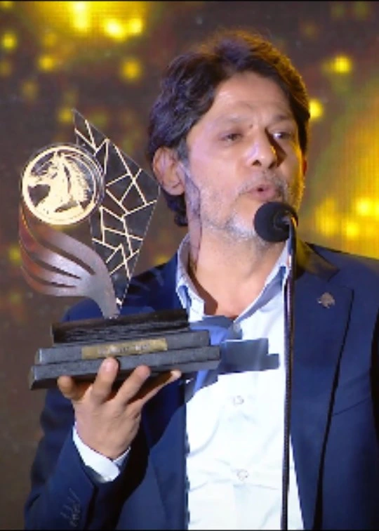 Moein Shreif holds an award while speaking into a microphone on the CAEL stage in 2025.